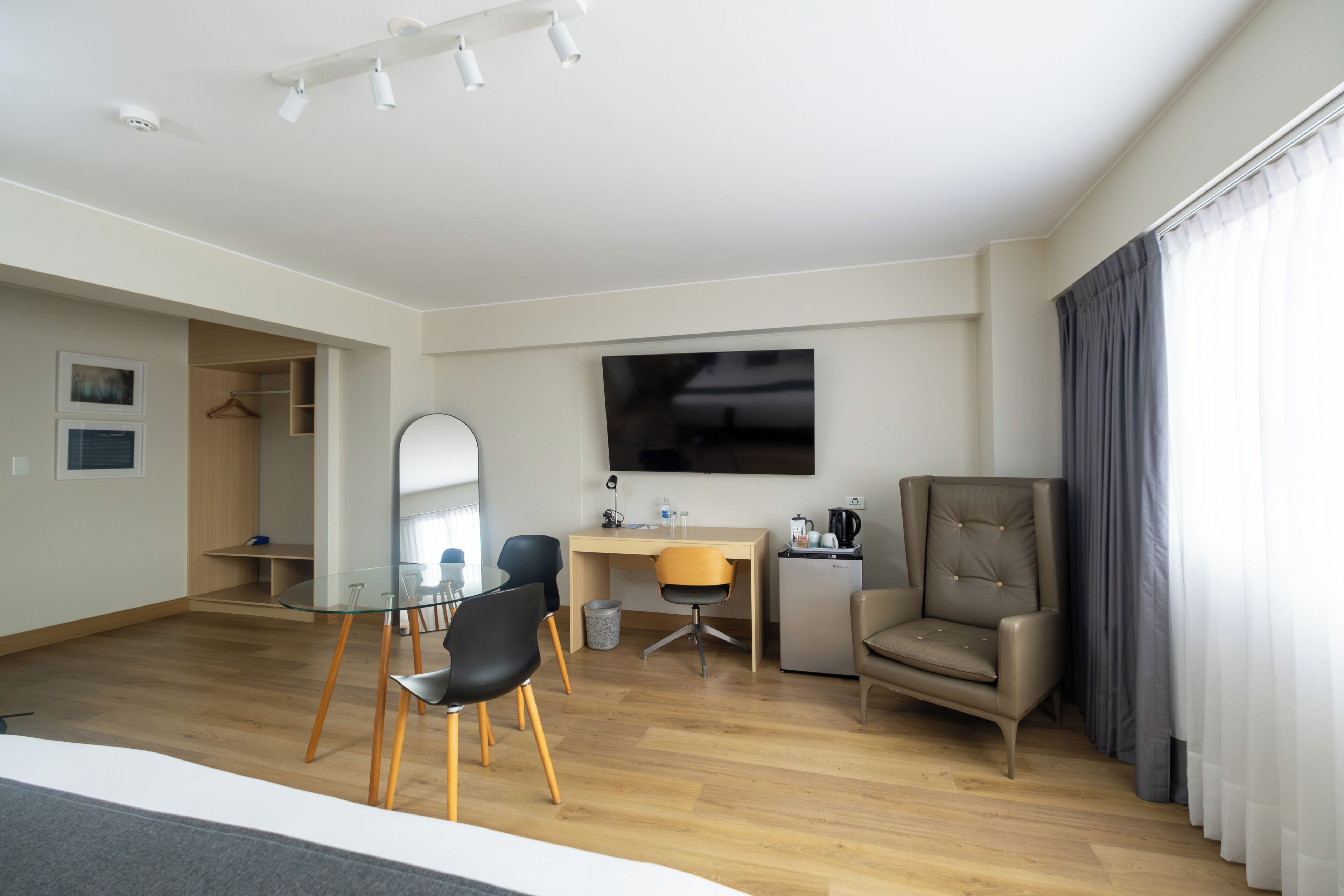 A modern hotel room with a bed, a desk, a chair, a TV, and a wardrobe.