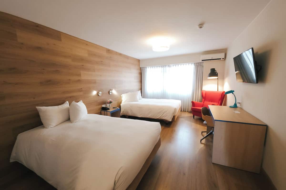 Habitación de hotel con dos camas, un escritorio, una silla, un televisor y una ventana con cortinas.