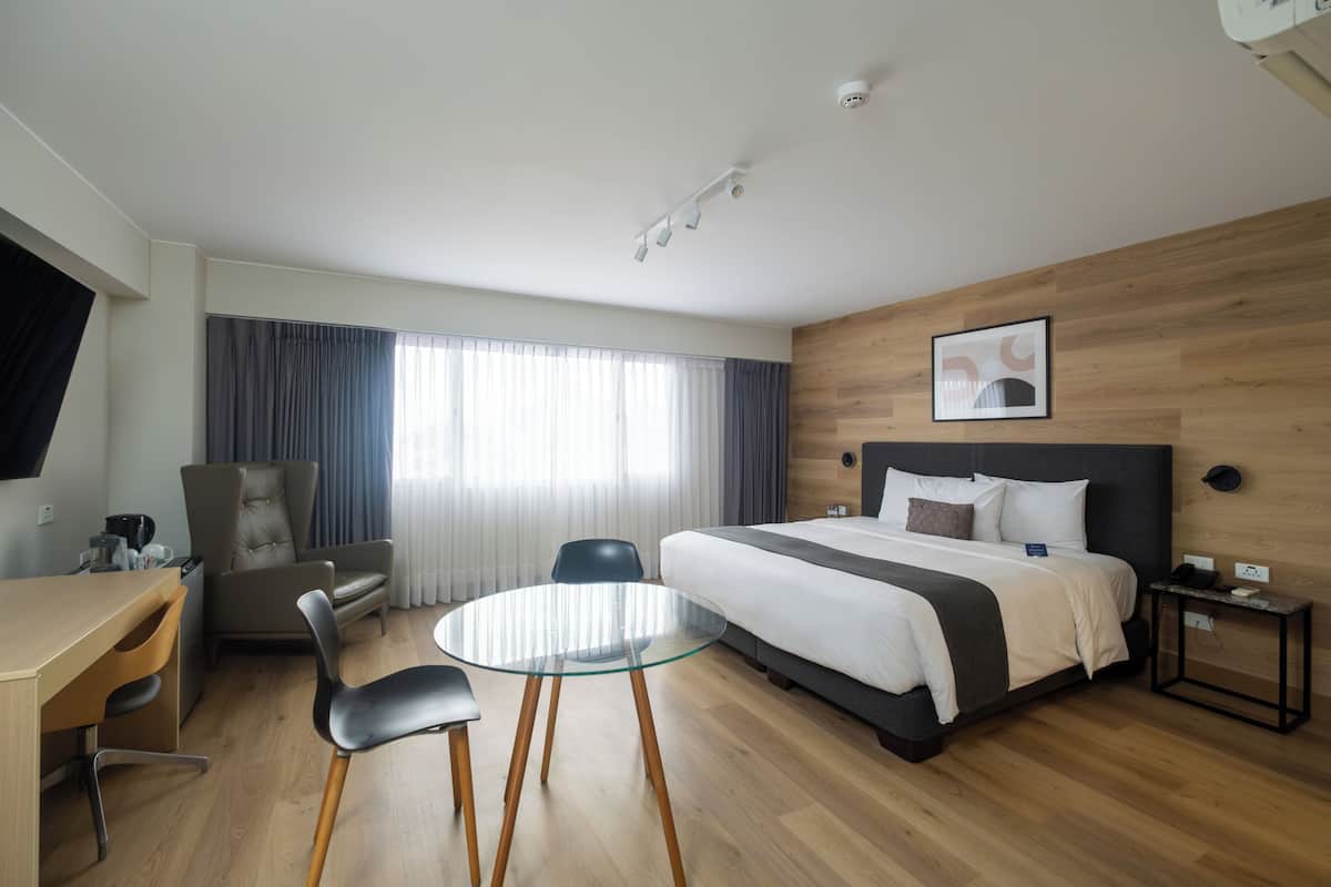 Habitación de hotel con cama, escritorio, sillas y una mesa redonda de vidrio.
