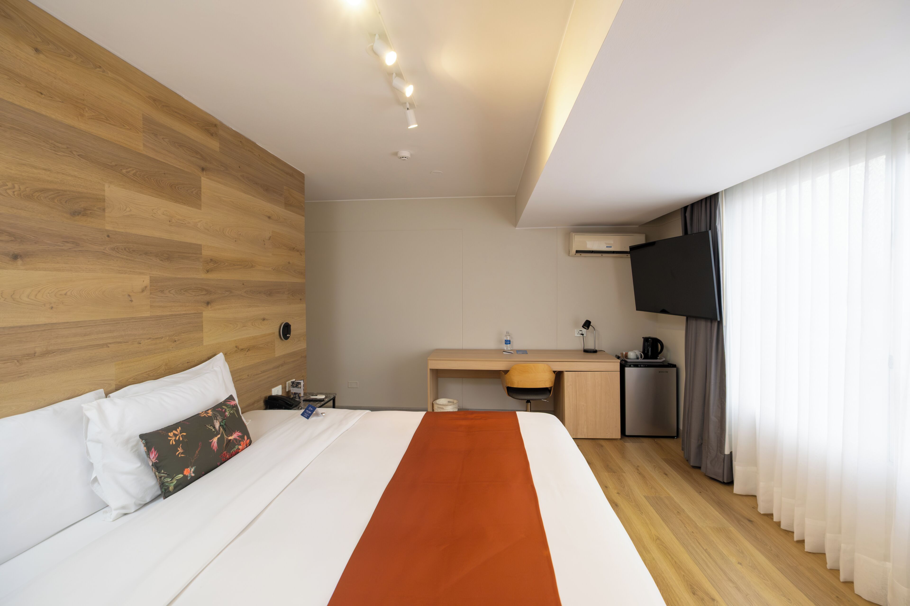 A hotel room with a bed, a desk, a television, and a kitchenette.