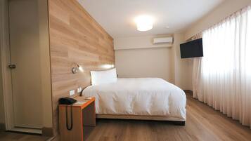 A modern hotel room with a wooden accent wall, a single bed, a bedside table with a telephone, and a flat-screen TV mounted on the wall.