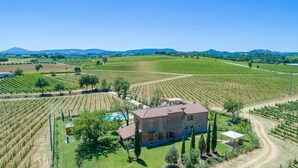 A large, rustic stone building surrounded by expansive vineyard fields, with a clear view of distant mountains.