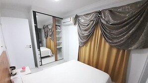 A bedroom with a bed, a wardrobe, a mirror, and a window with curtains. - 229, Apartamento 2 Dormitórios em Local Agradável (SC)