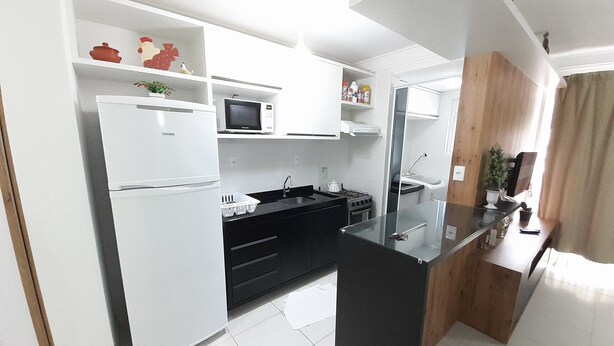 A modern kitchen with white cabinetry, a black countertop, and a built-in microwave. - 229, Apartamento 2 Dormitórios em Local Agradável (SC)