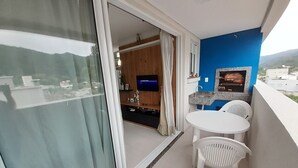 A balcony with a white table and chairs, a TV, and a kitchen area with a sink and countertop. - 229, Apartamento 2 Dormitórios em Local Agradável (SC)