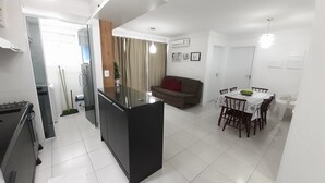 A modern kitchen with a central island, a dining area with a round table and chairs, and a living area with a sofa. - 229, Apartamento 2 Dormitórios em Local Agradável (SC)