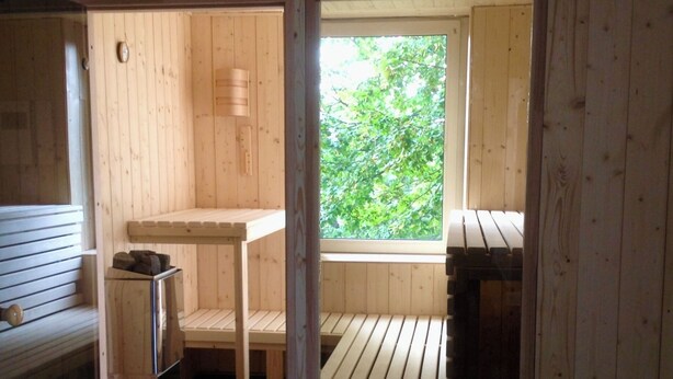 Ein Holzsaunaraum mit Bänken, einem Tisch und einem Fenster mit Blick ins Grüne.
