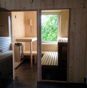 Ein Holzsaunaraum mit Bänken, einem Tisch und einem Fenster mit Blick ins Grüne.