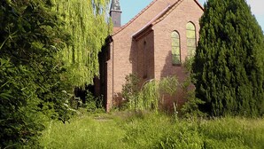 Ein Backsteinhaus mit Bogenfenstern und einem Turm, umgeben von dichtem Grün.