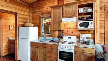 A compact kitchen with wooden cabinets, a refrigerator, a microwave, a stove, and a sink.