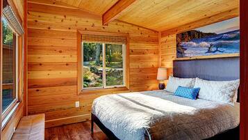 Een slaapkamer in een houten chalet met een bed, een bankje, een raam en een landschap op een schilderij.