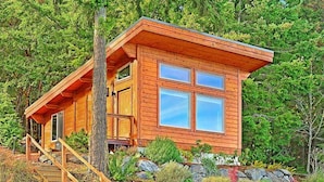 A wooden cabin with a balcony, surrounded by trees and a rocky garden.
