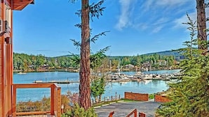 A wooden deck leading to a marina with boats, surrounded by tall trees and a clear blue sky.