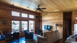 A cozy cabin interior with a dining area, sofa, TV, and a fireplace.