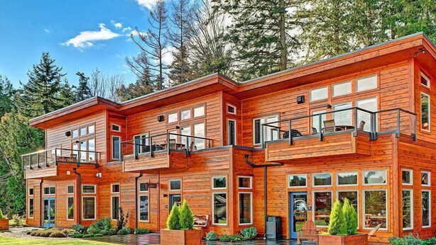 A modern wooden cabin with multiple levels, large windows, and outdoor seating areas.