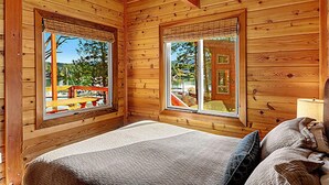 A wooden cabin room with a bed, two windows, and a view of a playground. - Snug Harbor Resort and Marina - Two Bedroom Water View Cabin, Queen Beds (Friday Harbor)