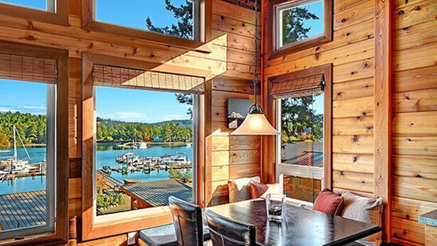 Una cabaña con comedor, ventanas amplias y vista a un lago con barcos.