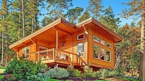 Una cabaña de madera con balcón, rodeada de árboles y un jardín bien cuidado.
