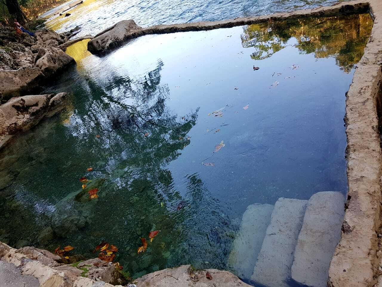 Cuerpo de agua clara con reflejos de árboles y un borde de hormigón.