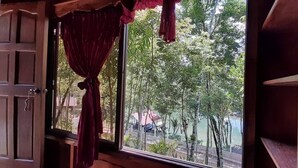 Ein Zimmer mit großem Fenster, Vorhängen und Blick auf Bäume sowie ein Gebäude in der Ferne.