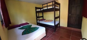A room with two bunk beds, a bed with a leaf-patterned bedspread, and a door. - Posada Las Marias (San Agustin Lanquin)