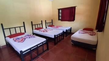 Una habitación con tres camas individuales, cada una con una almohada roja y una manta estampada.