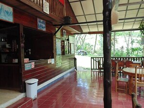 A covered outdoor seating area with wooden tables and chairs, a trash bin, and a staircase leading to an upper level. - Posada Las Marias (San Agustin Lanquin)