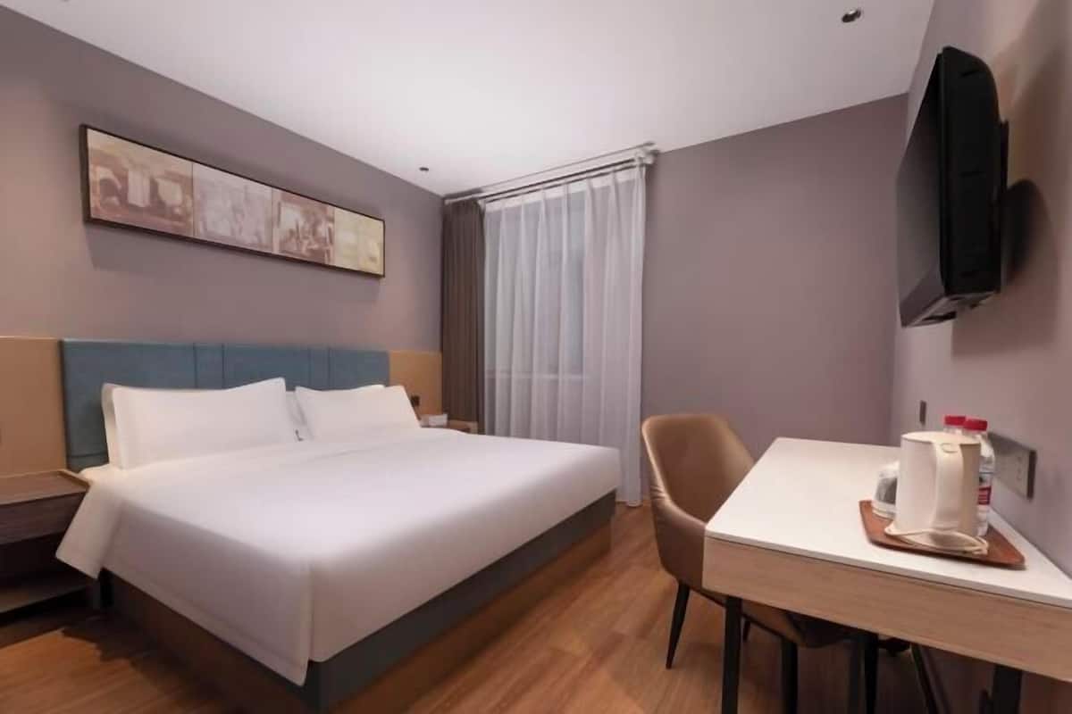A hotel room with a bed, a desk, a chair, a television, and a window with curtains.