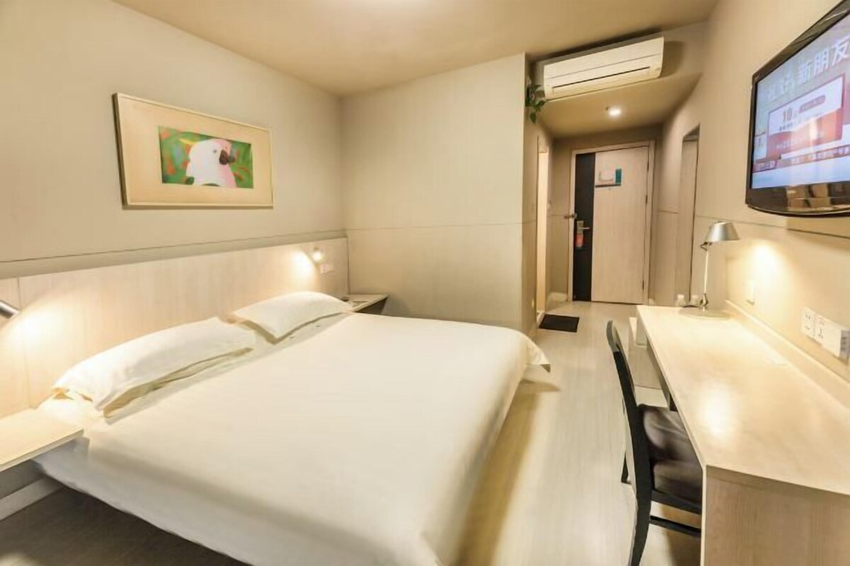 Quarto de hotel com cama, mesas de cabeceira, escrivaninha, cadeira, ar condicionado, televisão e um quadro na parede.