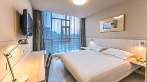 A hotel room with a large bed, a desk with a lamp, a TV mounted on the wall, and a window with curtains. - Jinjiang Inn (Wujiang Zhongshan North Road Pedestrian Street) (Suzhou)