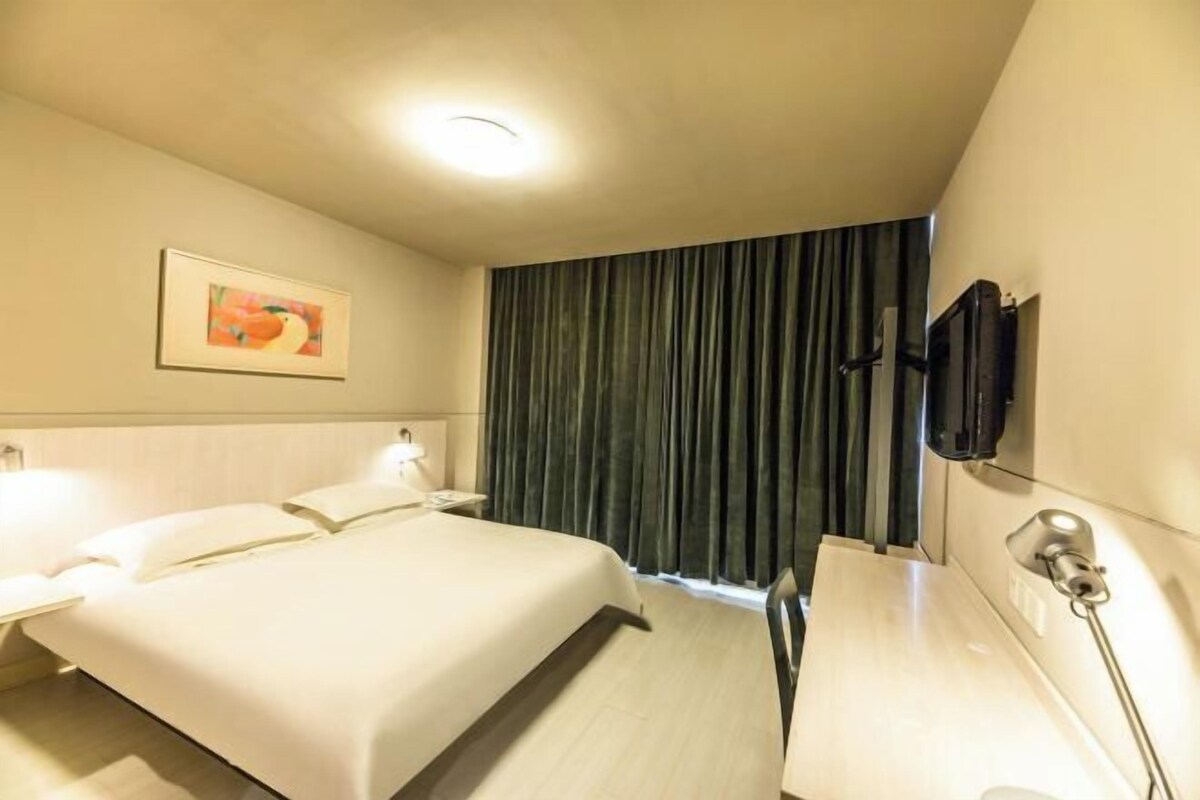 Quarto de hotel com cama, mesas de cabeceira, televisão e um quadro na parede.