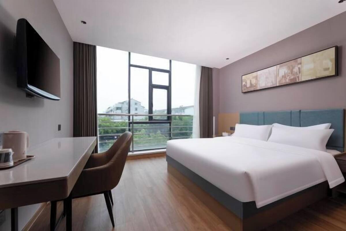 A modern hotel room with a large bed, a desk, and a TV mounted on the wall.