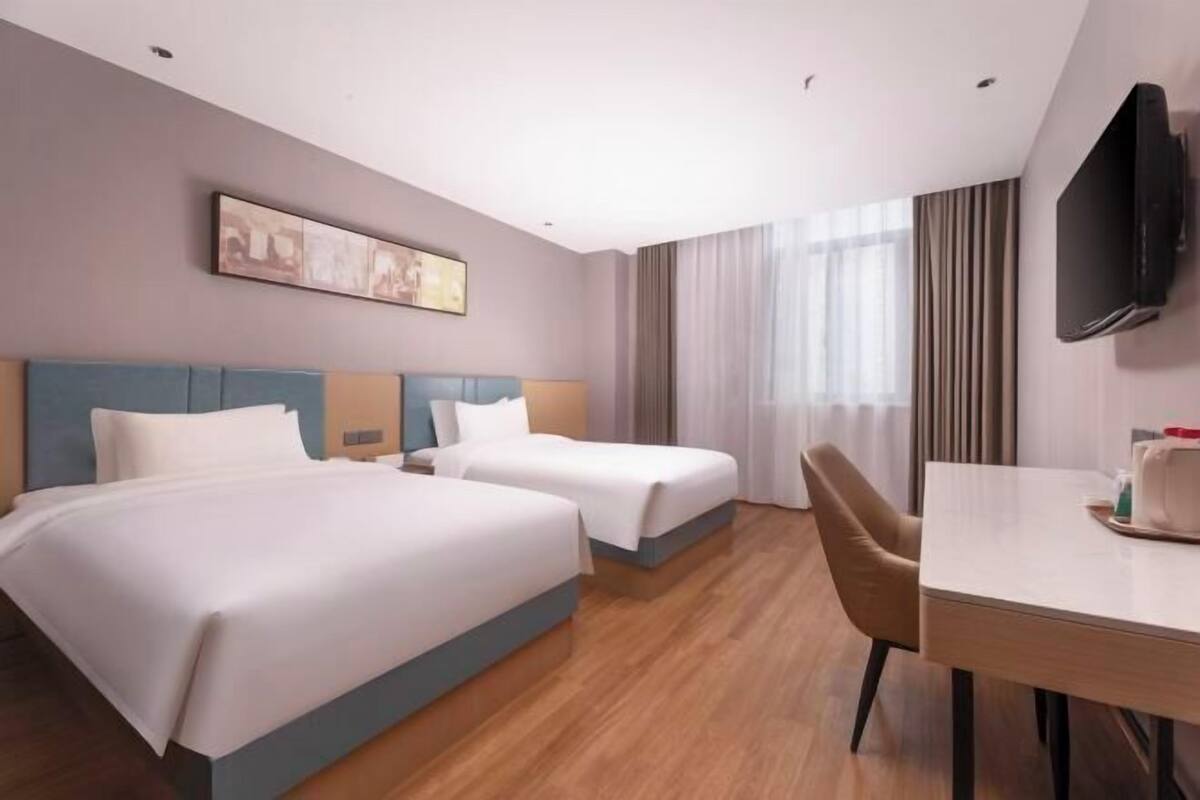 A hotel room with two beds, a desk, a chair, a flat-screen TV, and a painting on the wall.