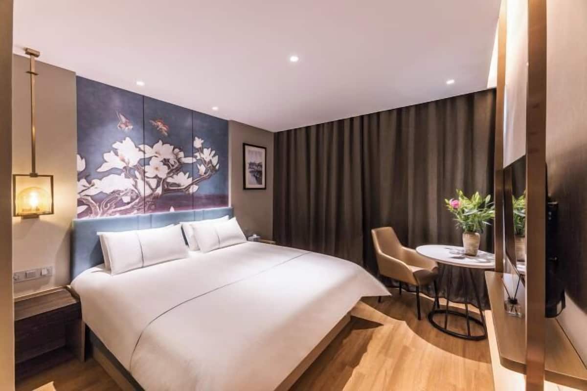 A modern hotel room with a large bed, a small dining table, and a wall-mounted TV.