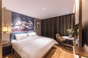 Quarto de hotel moderno com uma cama grande, uma pequena mesa de jantar e uma TV fixada na parede.