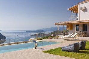 Una vila moderna amb piscina, mobiliari exterior i vistes al mar.