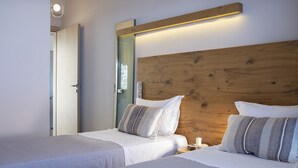 Quarto de hotel com duas camas, cabeceiras de madeira e uma mesa de cabeceira com uma vela.