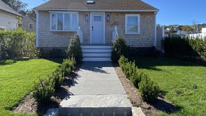 A single-story house with a front porch, a small front yard with a pathway, and a clear blue sky. - LOCATION  & QUALITY! Right in town, freshly renovated, near everything u need! (Tisbury)