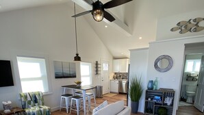 A spacious living room with a large sofa, a dining area with a table and chairs, a kitchen with white cabinets, and a ceiling fan. - LOCATION  & QUALITY! Right in town, freshly renovated, near everything u need! (Tisbury)