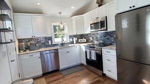 A modern kitchen with white cabinets, stainless steel appliances, and a wooden floor. - LOCATION  & QUALITY! Right in town, freshly renovated, near everything u need! (Tisbury)