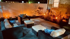 An outdoor patio area with wicker furniture, including sofas and ottomans, and a small tree. - LOCATION  & QUALITY! Right in town, freshly renovated, near everything u need! (Tisbury)