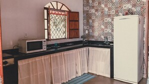 A compact kitchen with a microwave, a refrigerator, and a window with a wooden frame. - Casa de Campo Rosalinda (Sao Manuel de Carangola)