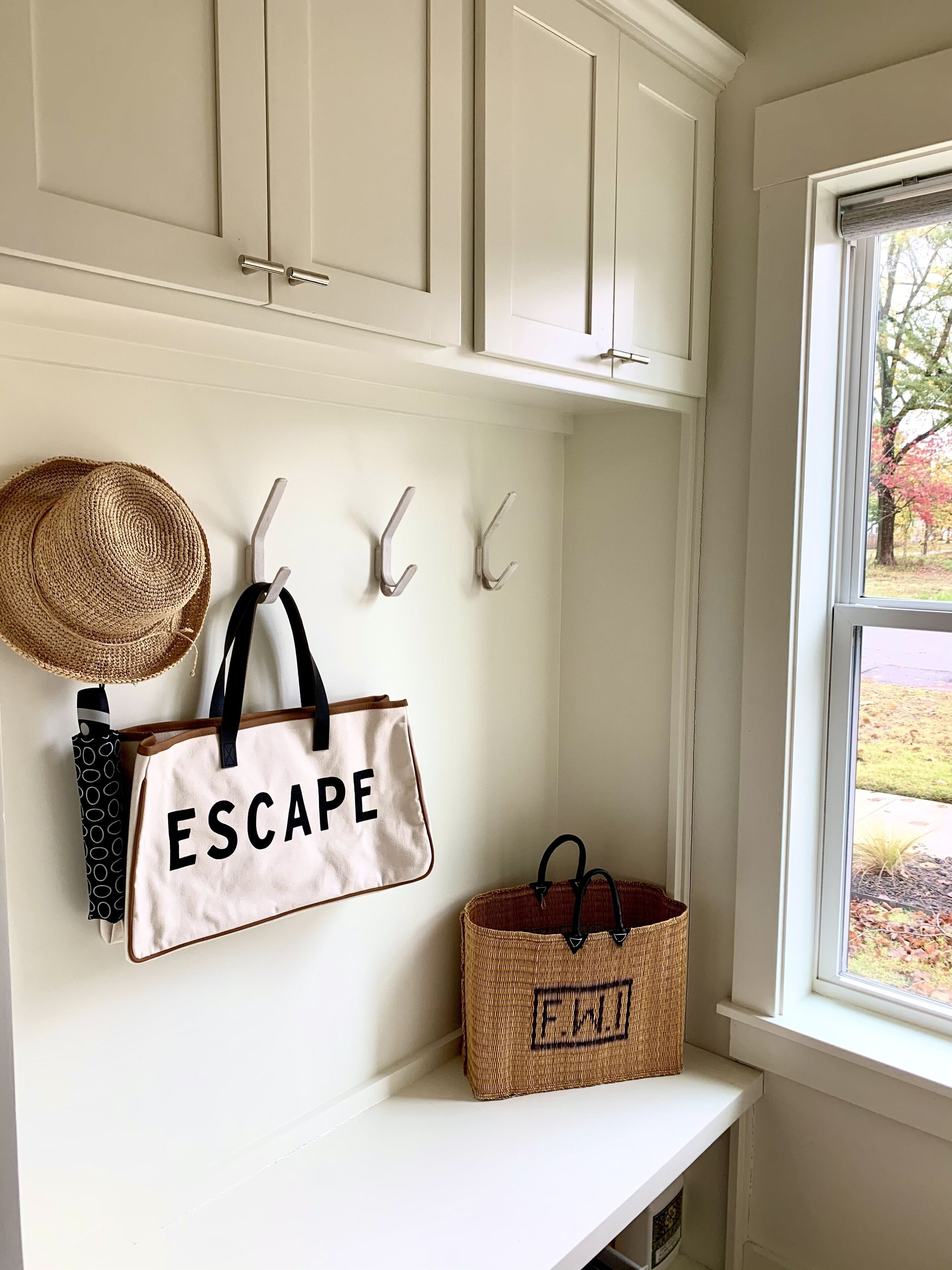 Un intérieur blanc avec une fenêtre, un chapeau, un sac fourre-tout sur lequel est écrit « ESCAPE », et un panier tressé portant les lettres « FW ».
