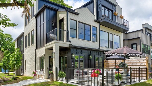 Ein modernes, zweistöckiges Haus mit Balkon, überdachter Terrasse und umzäunter Garten.
