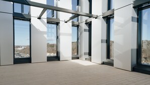 A modern interior with large windows, a wooden floor, and a view of buildings and trees.