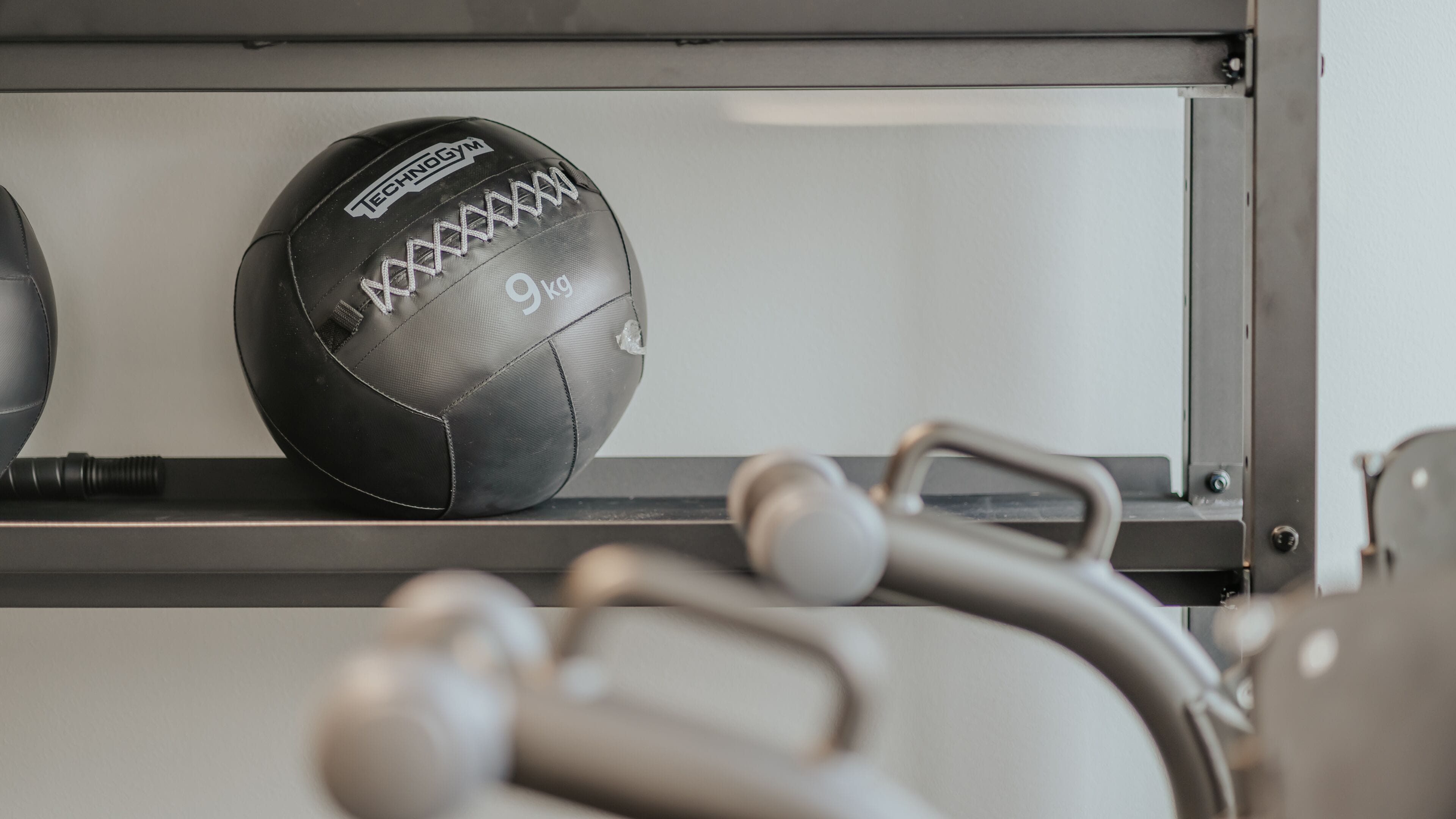 Un gimnasio con equipo de ejercicio y un balón deportivo negro que dice "Technogym" y "9kg".