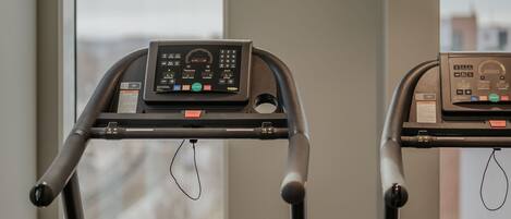 Two stationary exercise bikes with digital displays, positioned in front of a window with a view of buildings.