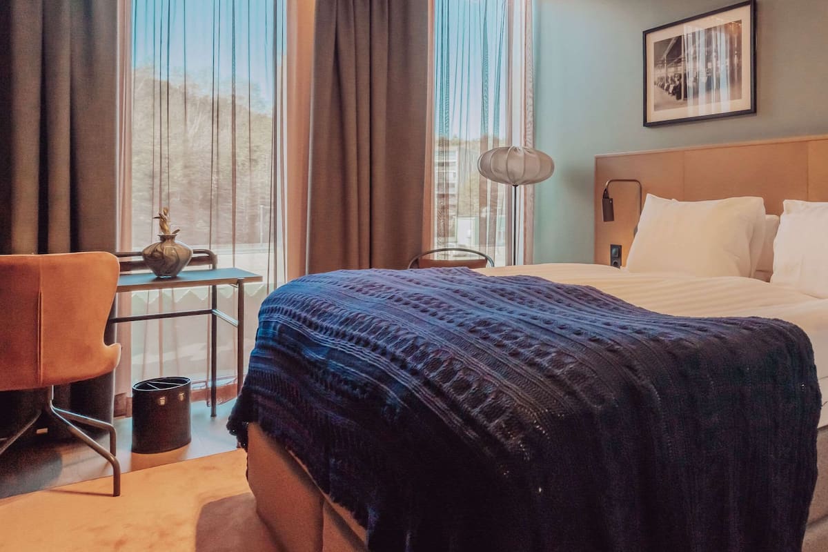 Een hotelkamer met een bed, een stoel, een tafeltje met een vaas en een foto aan de muur.