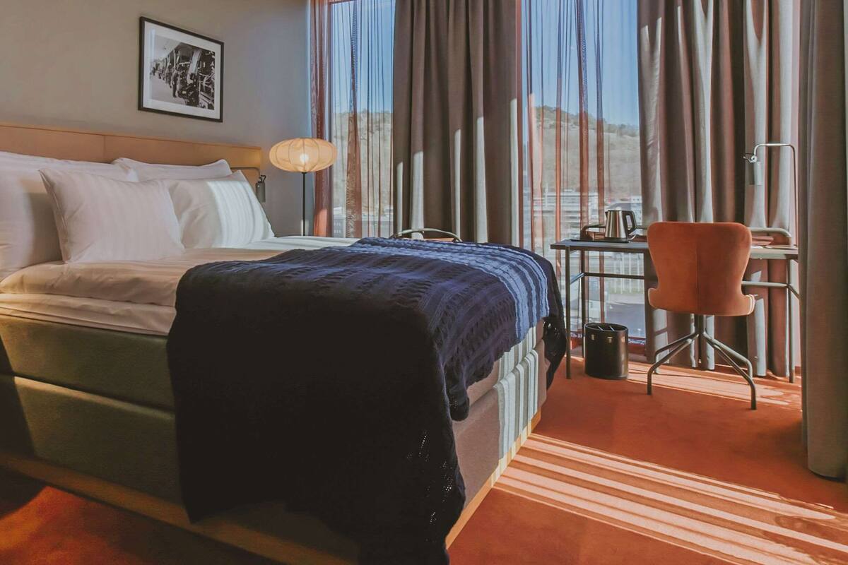 Hotelkamer met een bed, een bureau, een stoel, een lamp en een raam met gordijnen.