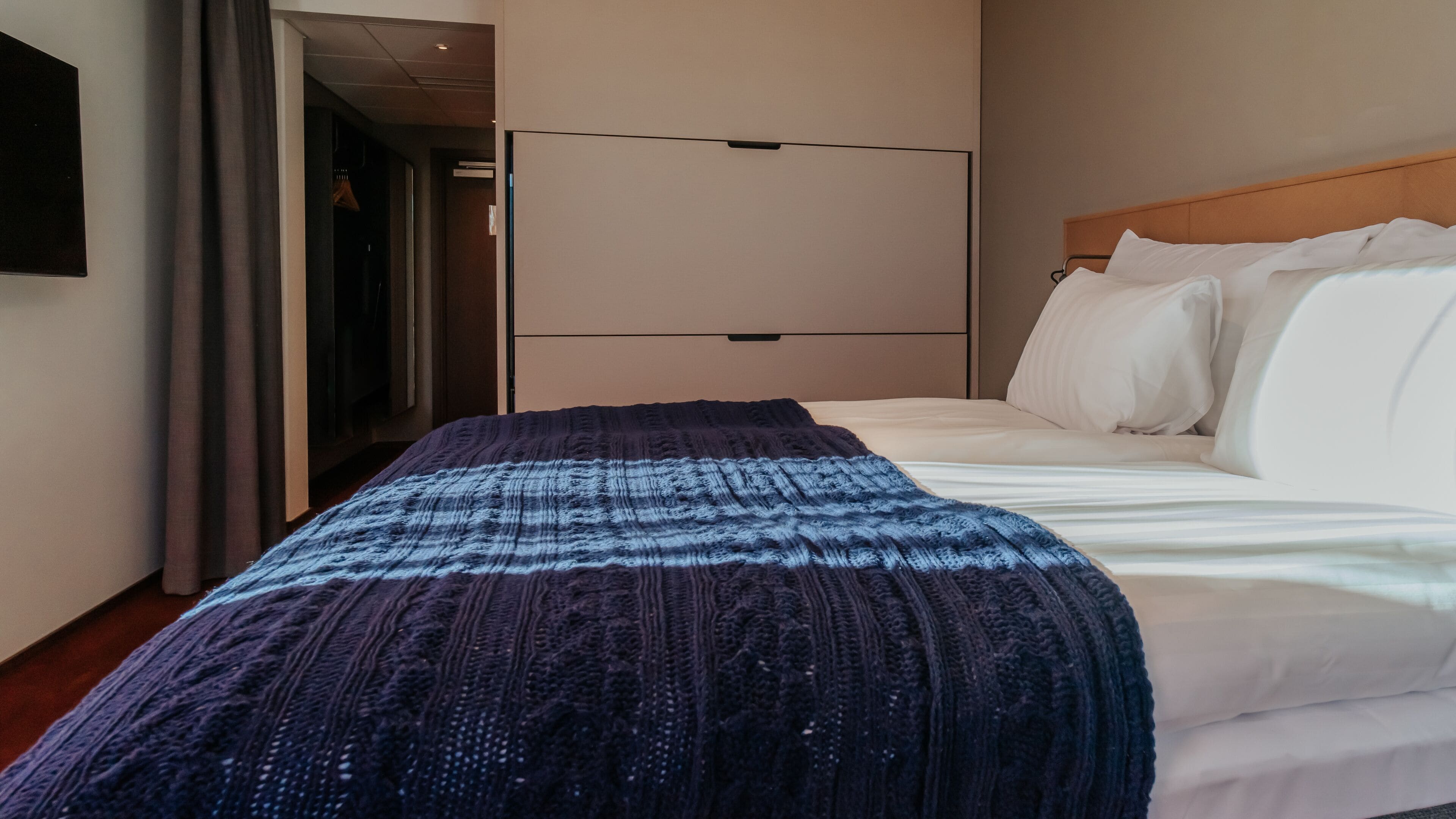 Una habitación de hotel con cama, armario y puerta que da a un pasillo.